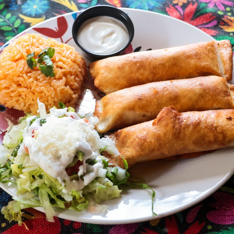 Three golden-brown flautas, Mexican rice, and a fresh salad with sour cream and cheese.