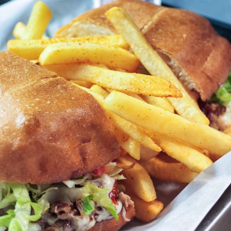 Two hearty sandwiches with meat, cheese, and lettuce, served with a generous portion of golden fries.